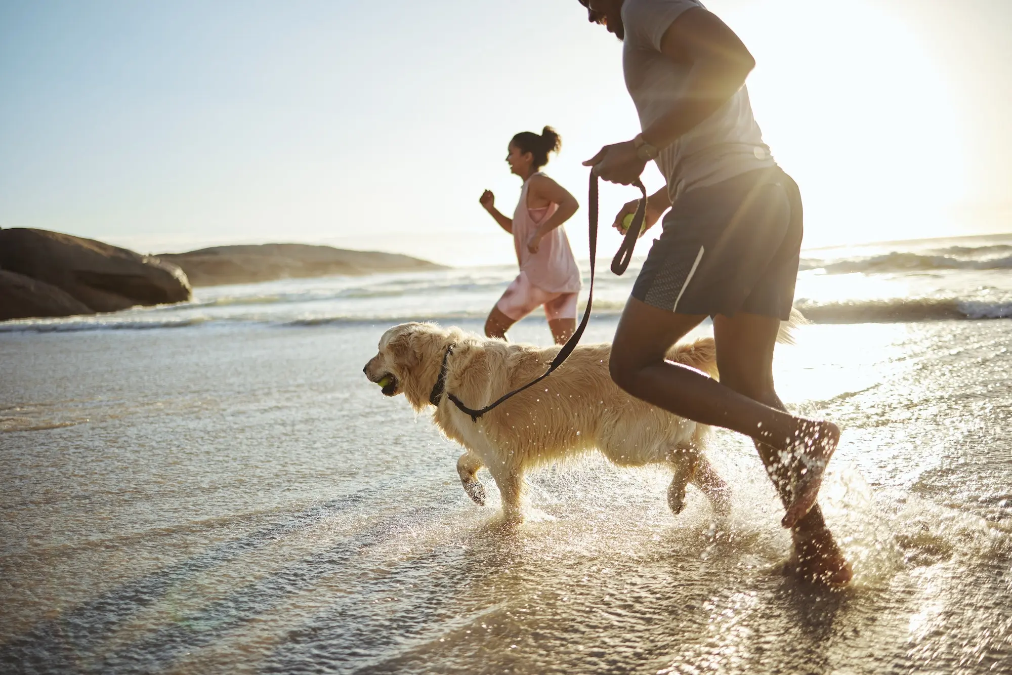 Running, dog and beach with a black couple and pet in the water while on holiday or vacation by the